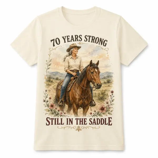 Flat front view of a light T-shirt with 70 Years Strong Still in the Saddle western horse lover 70th birthday design